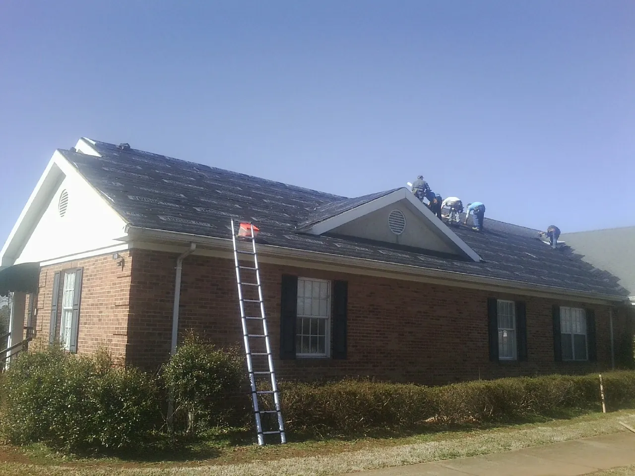 Crew tearing shingles off a brick ranch roof with a ladder set — Metal Roof Repair work by our crew in Washington Crossing