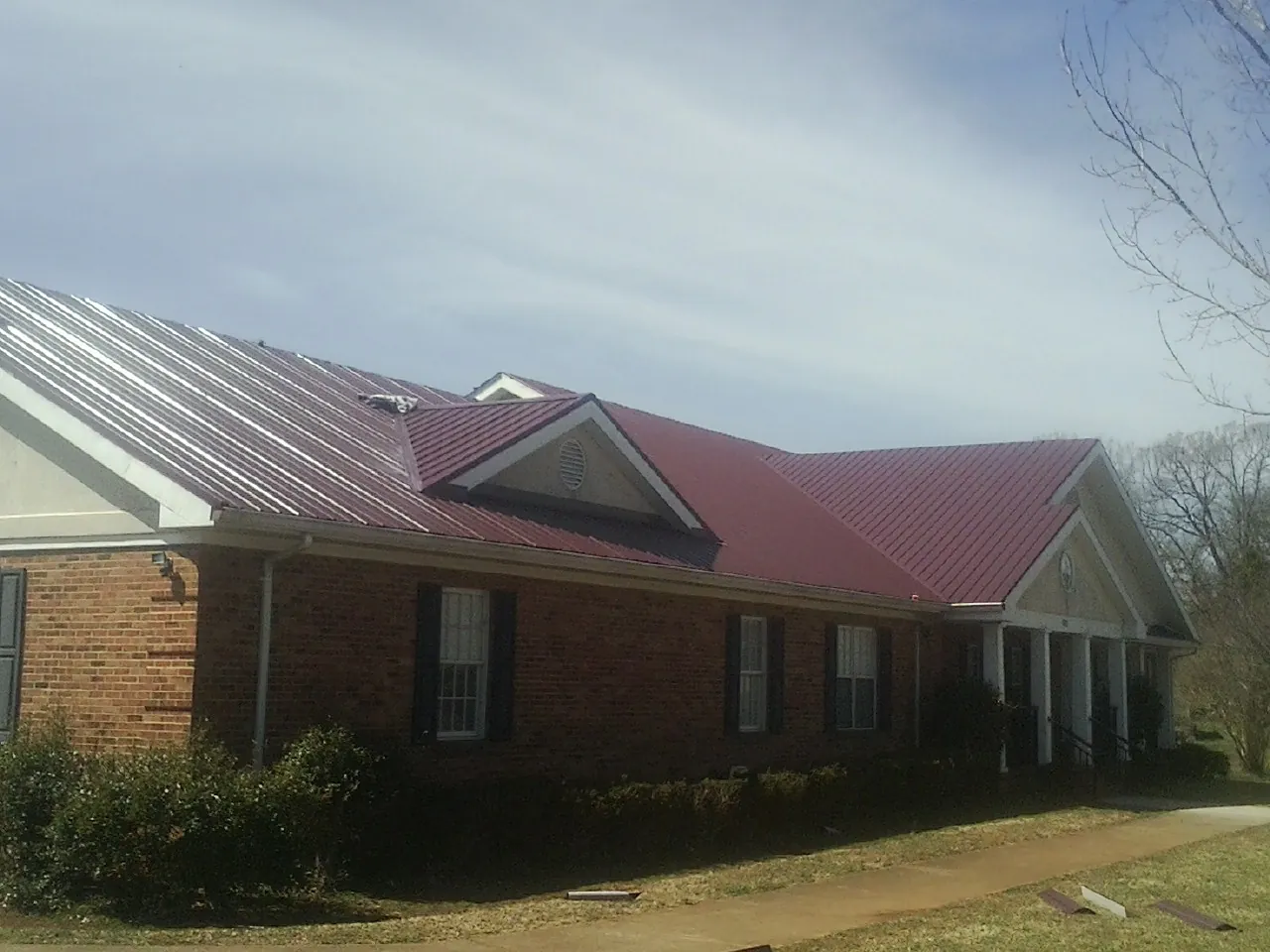 Red metal roof with gabled entries on a long brick building, from a Hail Damage Roof Repair job in Washington Crossing