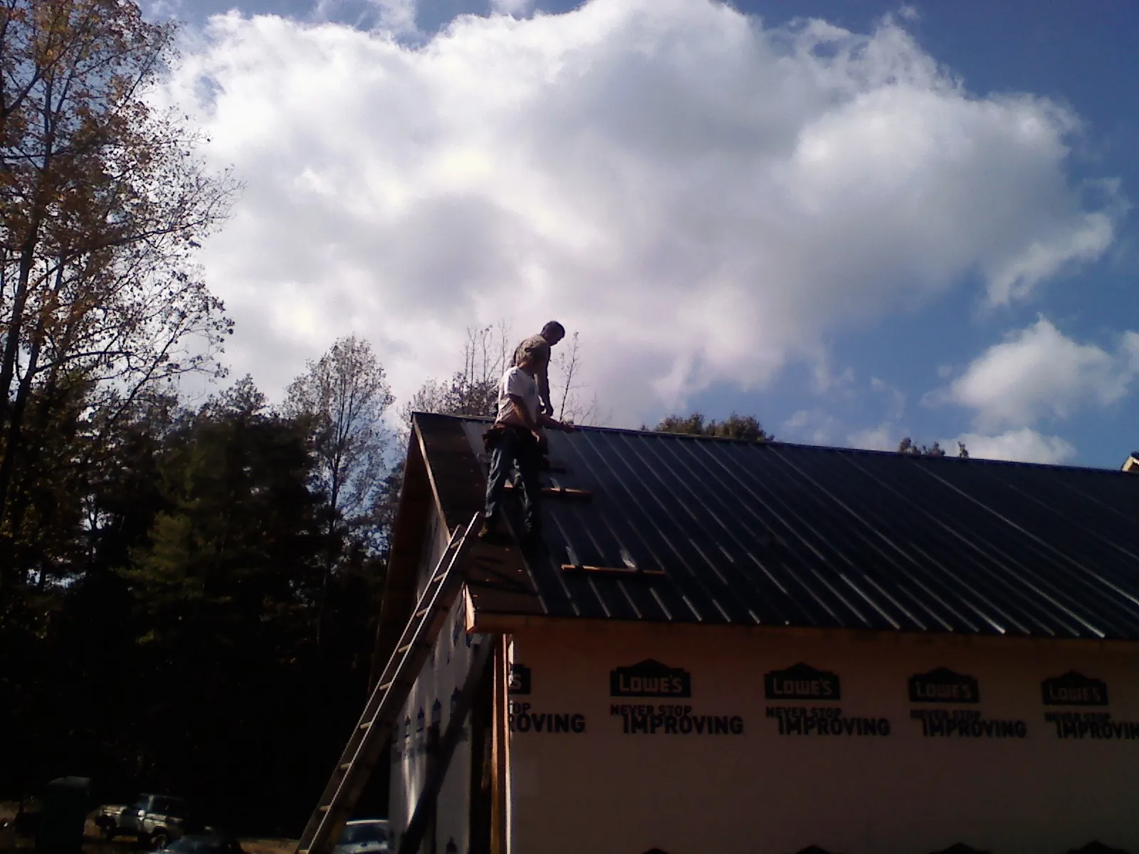 Roofer fastening dark metal panels high against a cloudy sky, from a Roof Inspection job in Washington Crossing