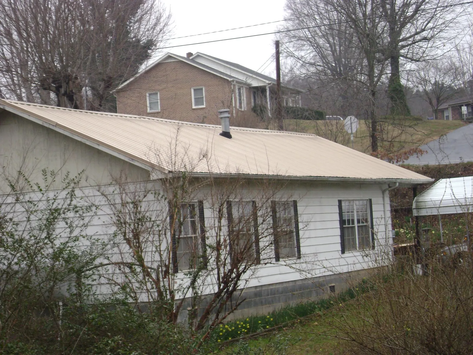 Tan metal roof on a white sided house set into a hillside — Commercial Roofing by Roofing Brothers in Washington Crossing